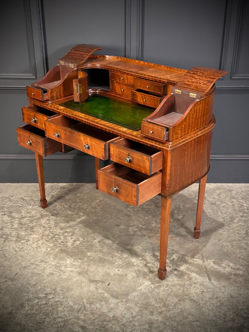 An inlaid mahogany Carlton House writing desk featuring a curved gallery with small drawers and cupboards above a green leather writing surface and square tapered legs. View VIII