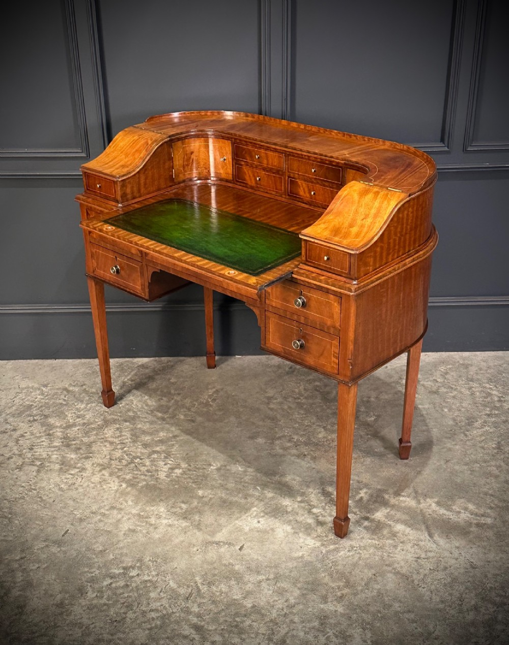 An inlaid mahogany Carlton House writing desk featuring a curved gallery with small drawers and cupboards above a green leather writing surface and square tapered legs. View IX