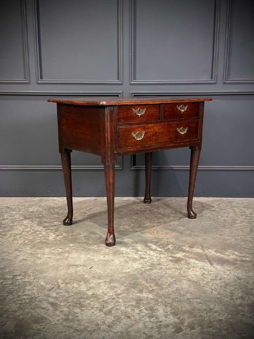 A Queen Anne dark oak lowboy featuring three drawers with brass backplate handles resting on slender cabriole legs with pad feet. View II