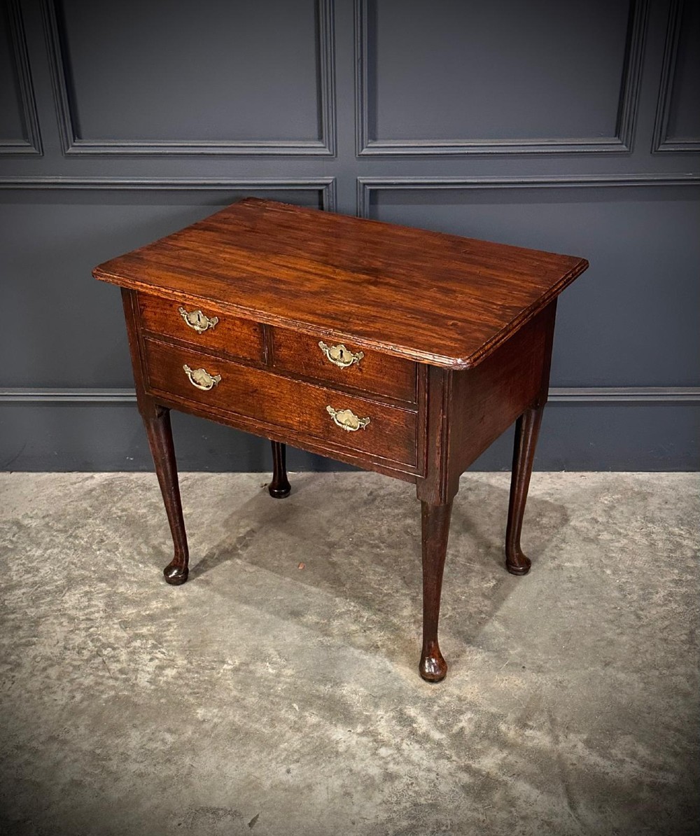 A Queen Anne dark oak lowboy featuring three drawers with brass backplate handles resting on slender cabriole legs with pad feet. View III