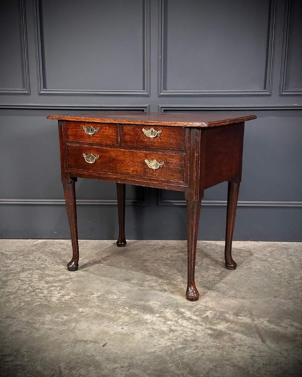 A Queen Anne dark oak lowboy featuring three drawers with brass backplate handles resting on slender cabriole legs with pad feet. View XI