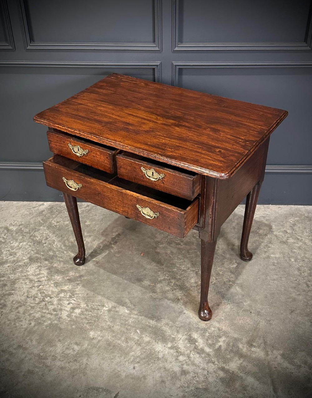 A Queen Anne dark oak lowboy featuring three drawers with brass backplate handles resting on slender cabriole legs with pad feet. View XIII