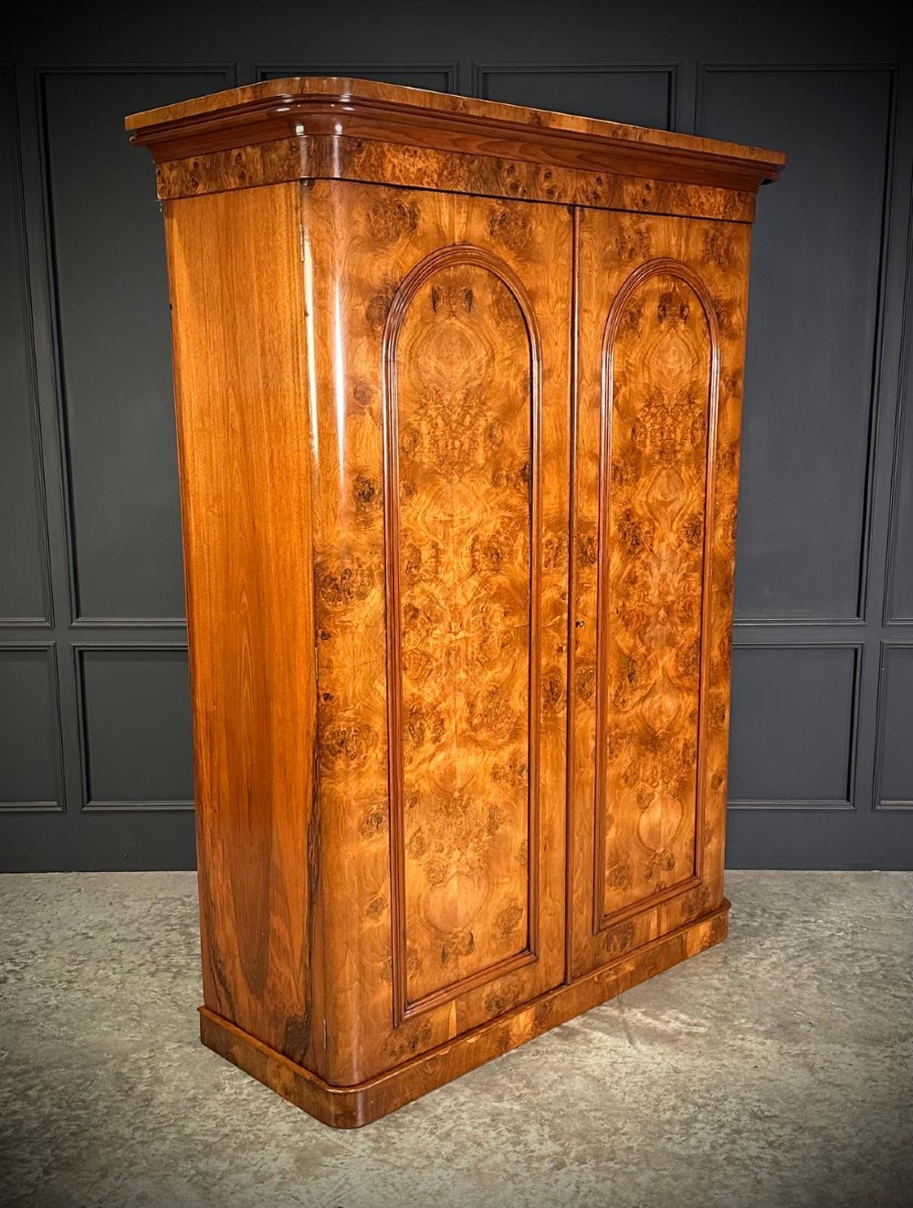 A Victorian double-door wardrobe crafted from figured burr walnut featuring arched door panels and a rounded moulded cornice.