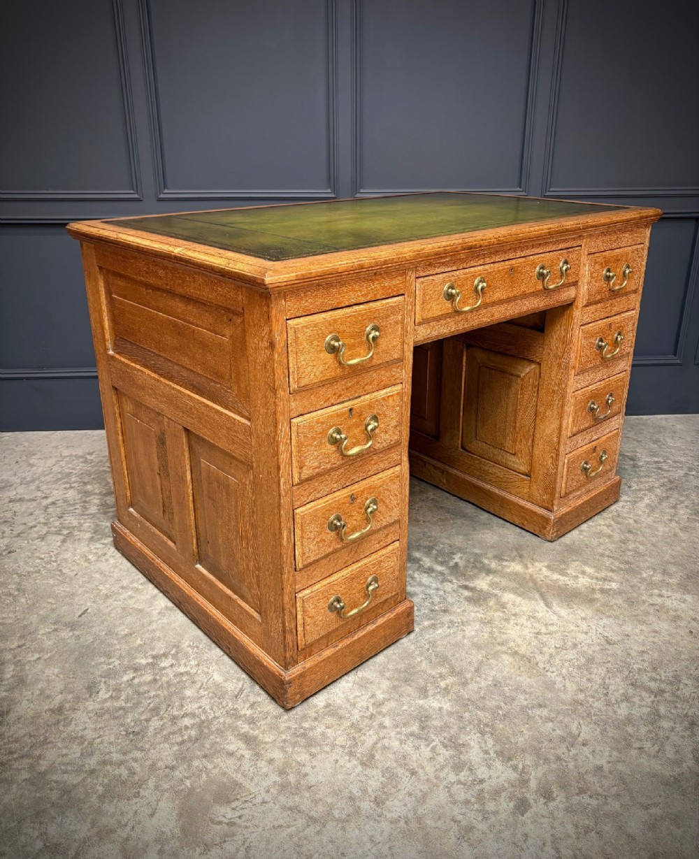 A 19th-century oak kneehole desk featuring nine drawers, brass drop handles, and a green leather inset writing top. View II