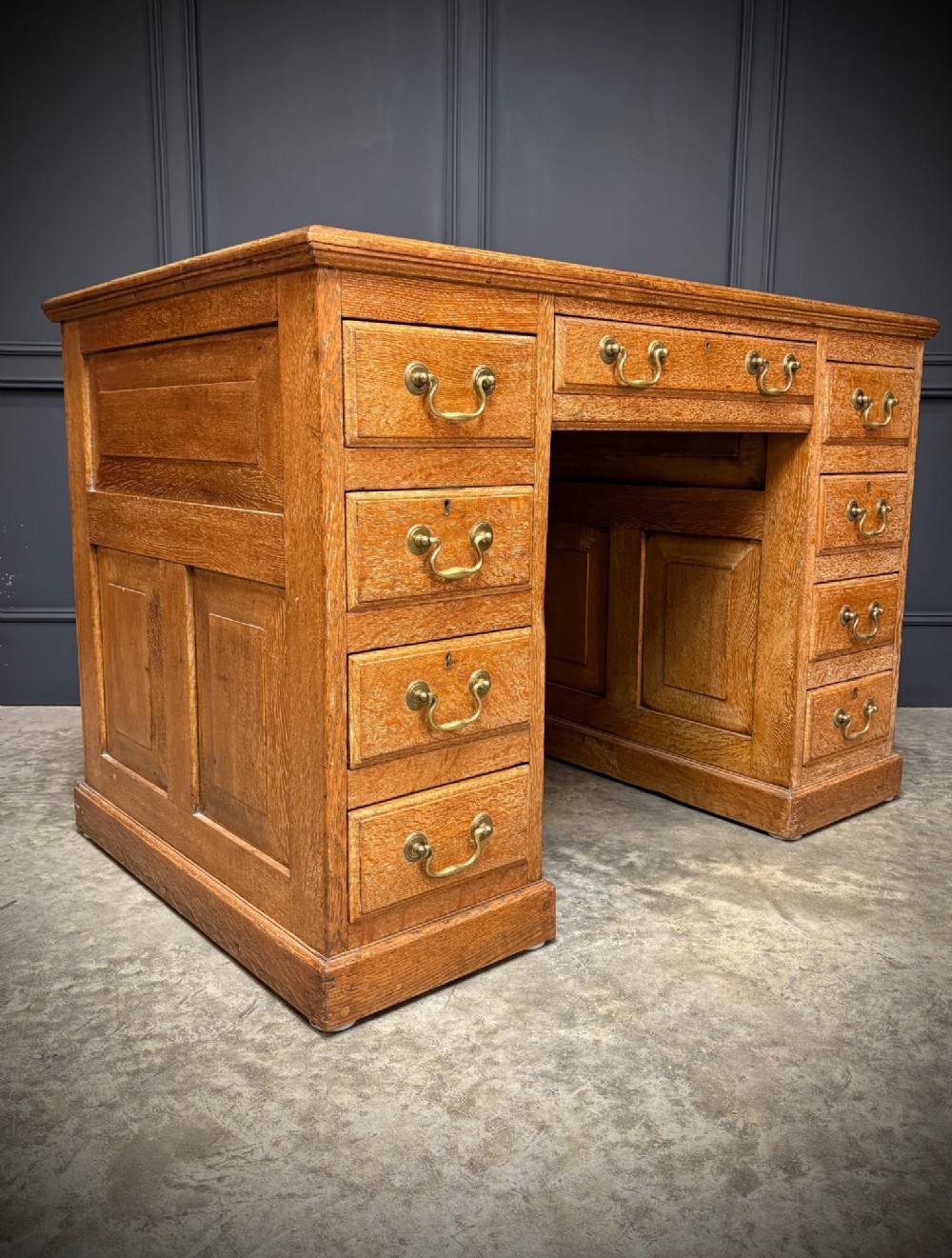 A 19th-century oak kneehole desk featuring nine drawers, brass drop handles, and a green leather inset writing top. View III