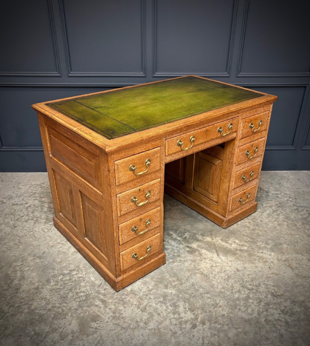 A 19th-century oak kneehole desk featuring nine drawers, brass drop handles, and a green leather inset writing top. View IV