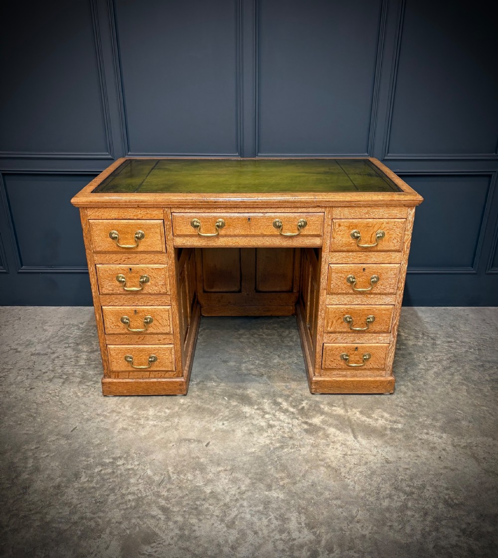 A 19th-century oak kneehole desk featuring nine drawers, brass drop handles, and a green leather inset writing top.