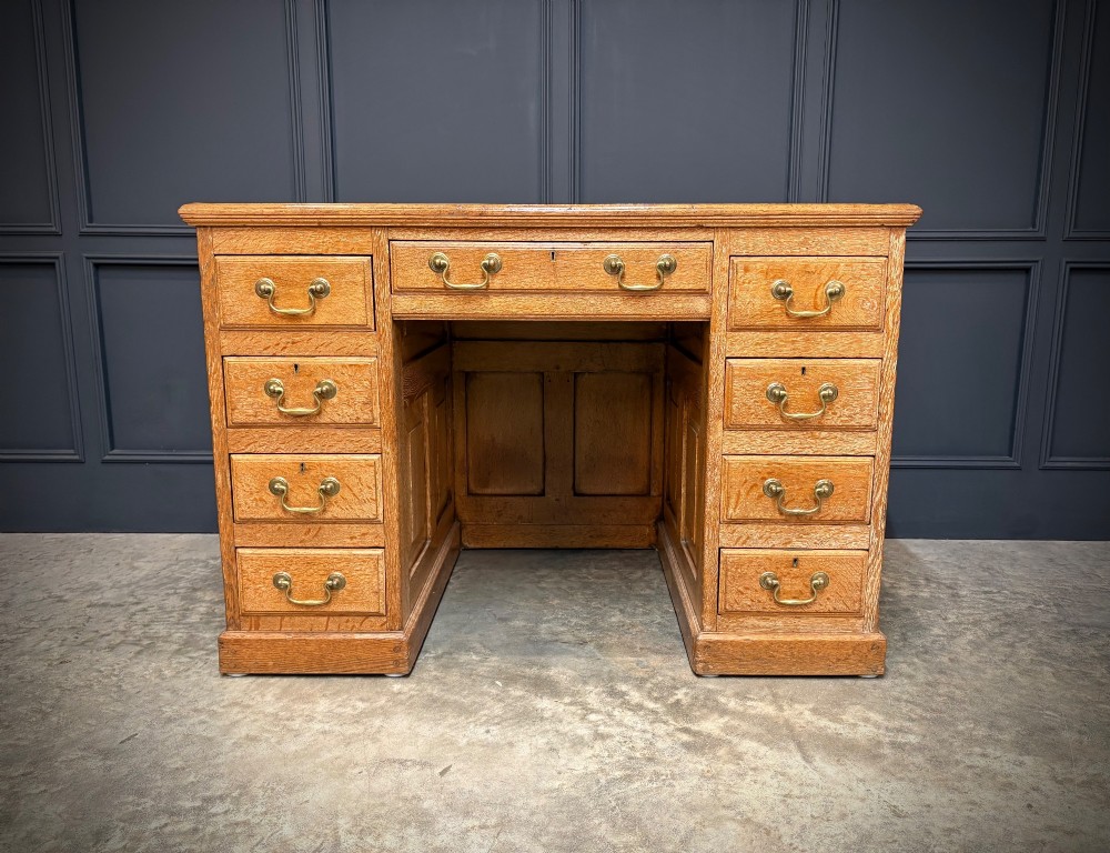 A 19th-century oak kneehole desk featuring nine drawers, brass drop handles, and a green leather inset writing top. View V