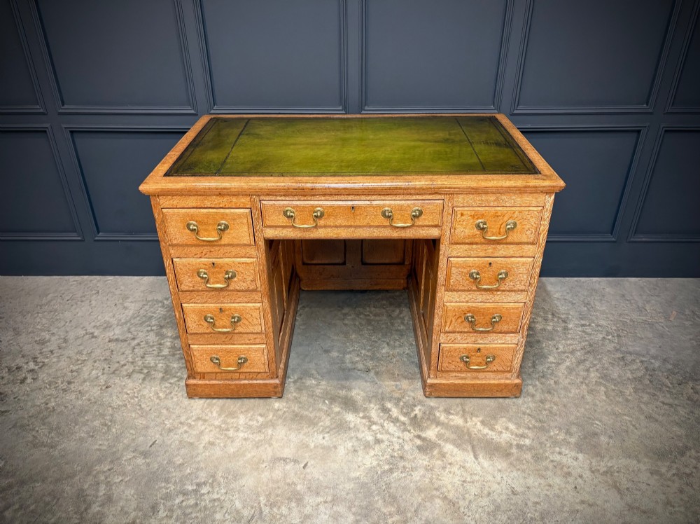 A 19th-century oak kneehole desk featuring nine drawers, brass drop handles, and a green leather inset writing top. View VI