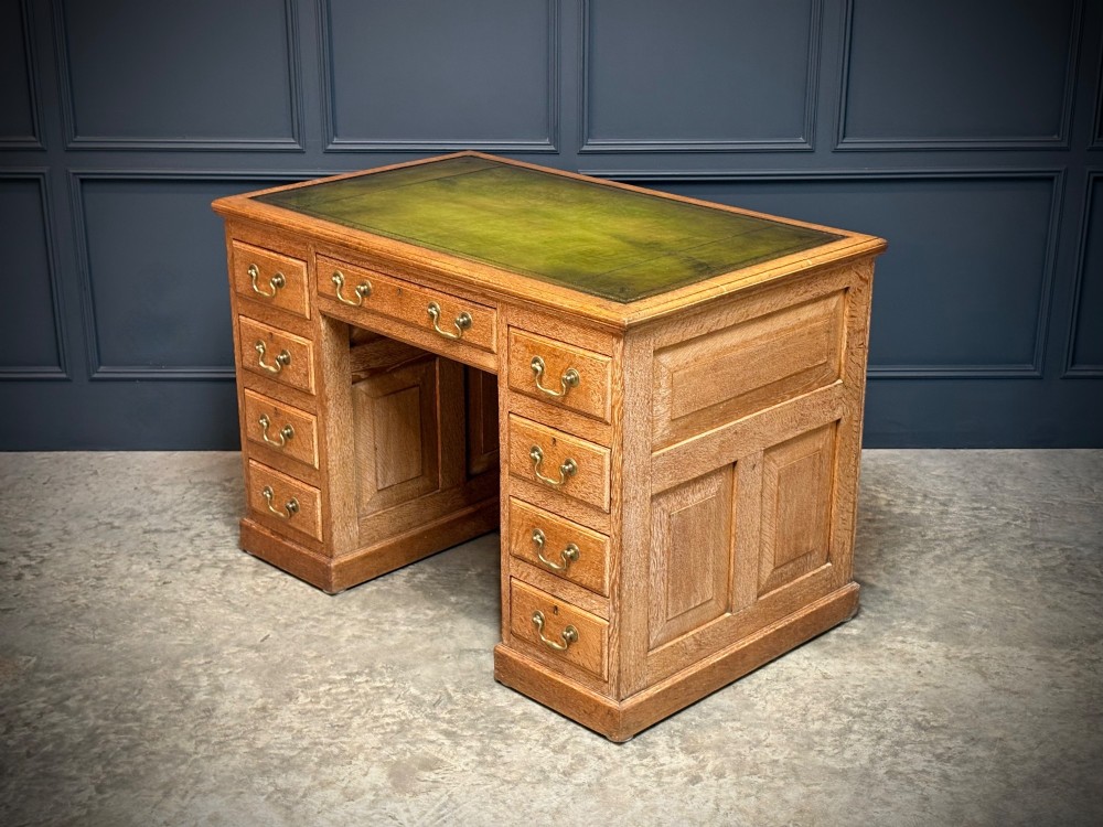 A 19th-century oak kneehole desk featuring nine drawers, brass drop handles, and a green leather inset writing top. View VII
