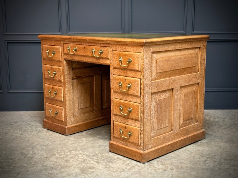 A 19th-century oak kneehole desk featuring nine drawers, brass drop handles, and a green leather inset writing top. View VIII