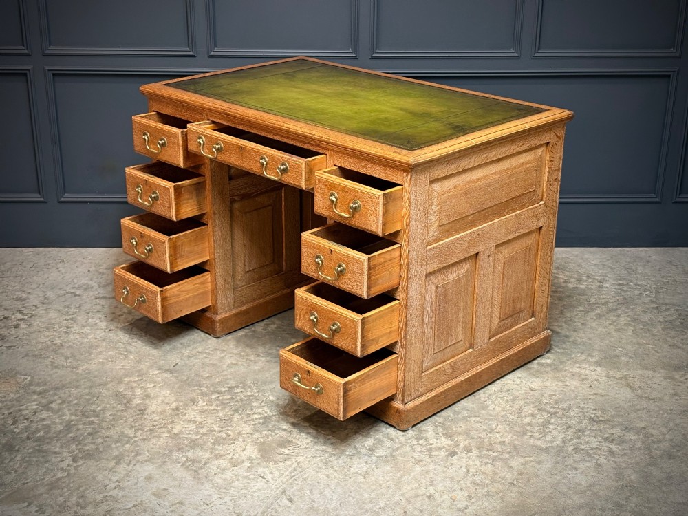 A 19th-century oak kneehole desk featuring nine drawers, brass drop handles, and a green leather inset writing top. View IX