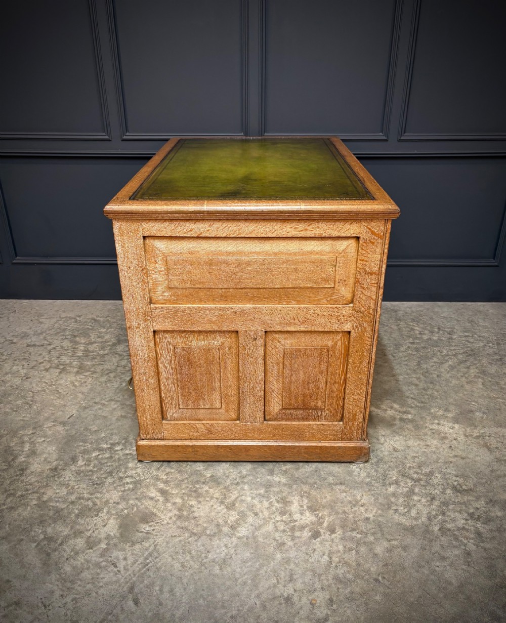A 19th-century oak kneehole desk featuring nine drawers, brass drop handles, and a green leather inset writing top. View X