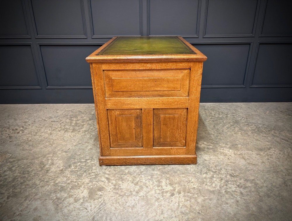 A 19th-century oak kneehole desk featuring nine drawers, brass drop handles, and a green leather inset writing top. View XIV