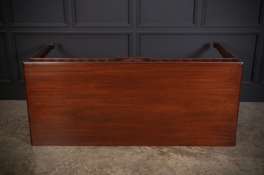 A large Sheraton style mahogany serving table featuring a rectangular top, frieze carved with drapery swags and a central urn relief, supported by four tapered fluted legs. View XIII