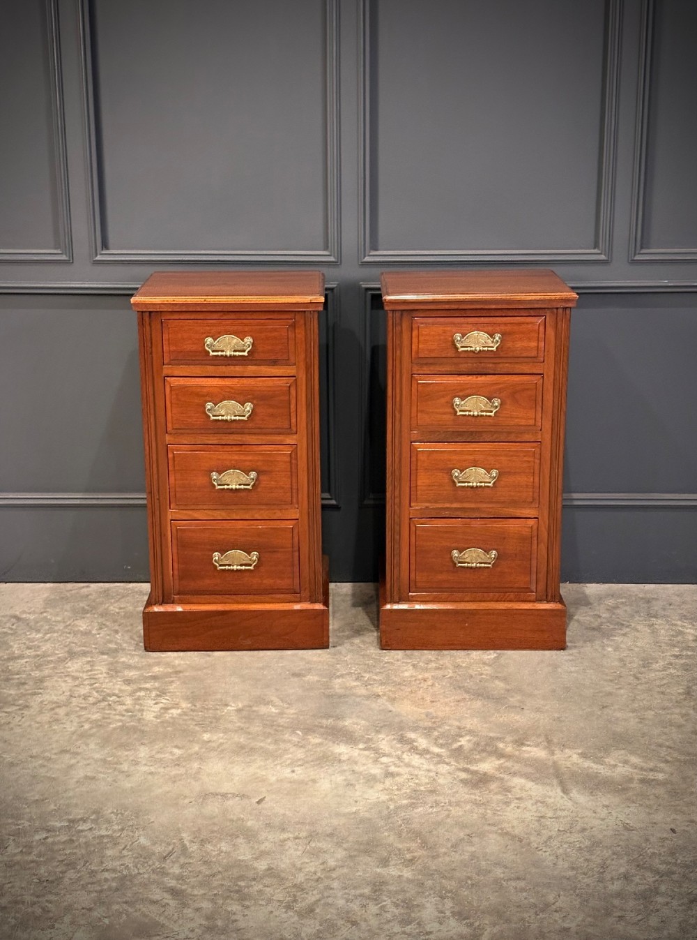 A pair of matching Victorian walnut bedside chests featuring four drawers each, brass drop handles, and a solid plinth base.