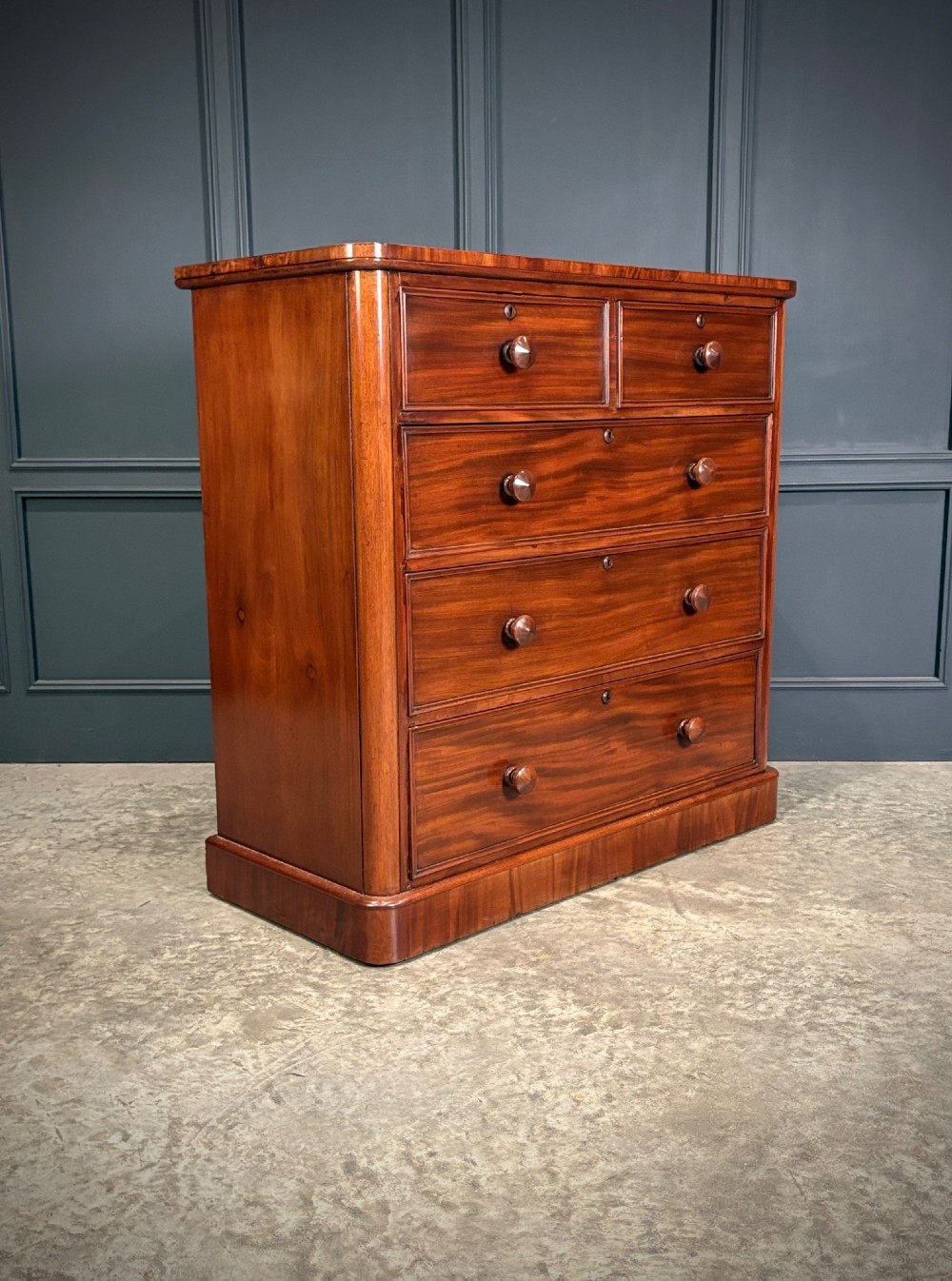 A Victorian mahogany chest of drawers with a two-over-three drawer arrangement, turned wooden knobs, rounded front corners, and a solid plinth base.