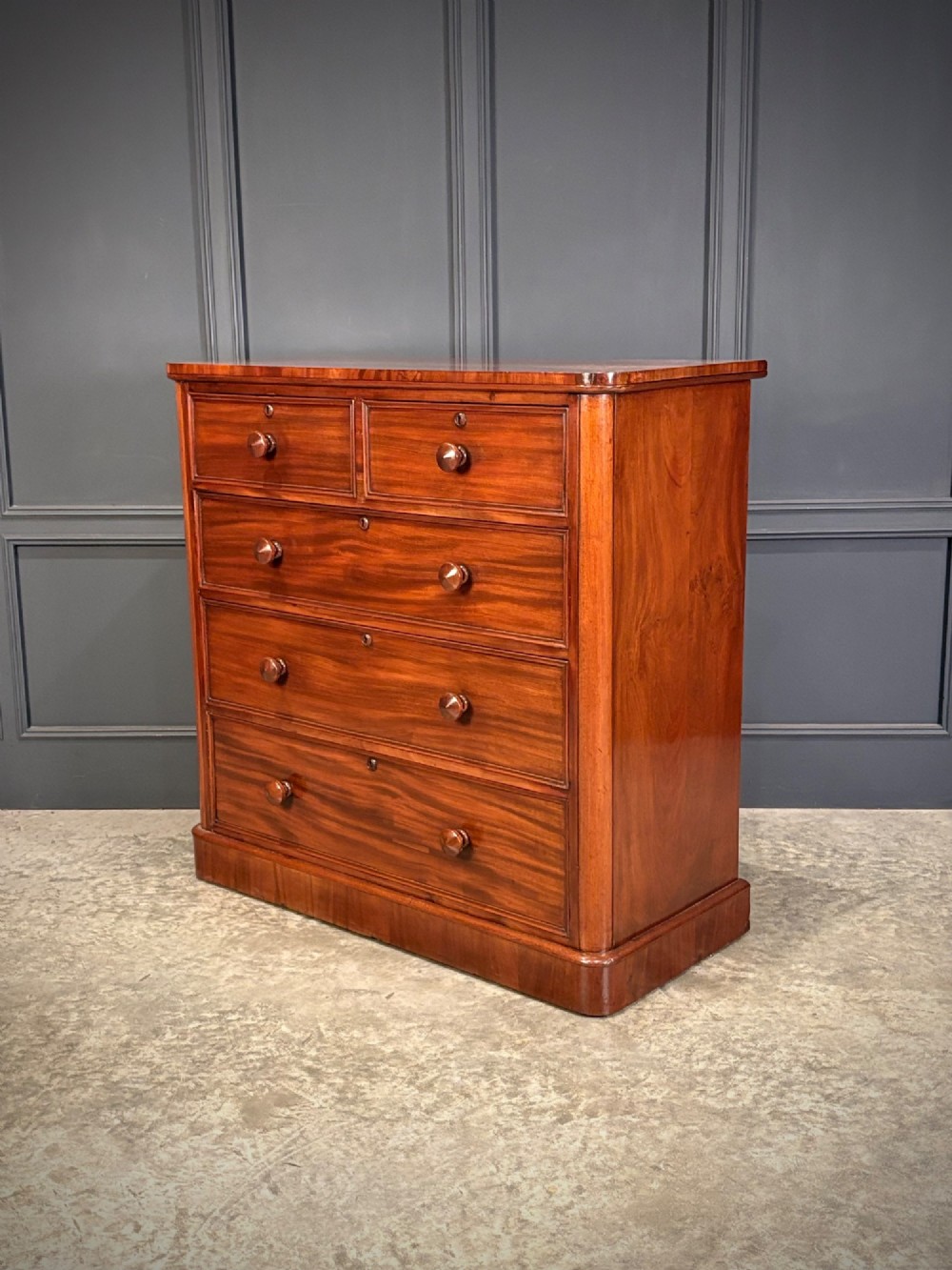 A Victorian mahogany chest of drawers with a two-over-three drawer arrangement, turned wooden knobs, rounded front corners, and a solid plinth base. View VII