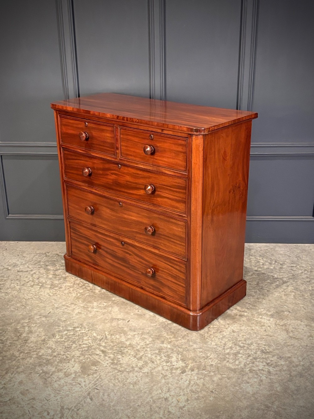 A Victorian mahogany chest of drawers with a two-over-three drawer arrangement, turned wooden knobs, rounded front corners, and a solid plinth base. View VIII