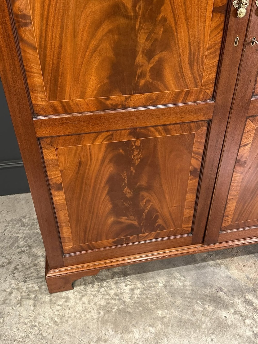 A tall Georgian style mahogany double wardrobe featuring flame mahogany door panels, a moulded cornice, and bracket feet. View II