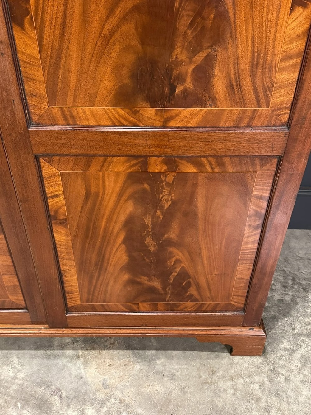 A tall Georgian style mahogany double wardrobe featuring flame mahogany door panels, a moulded cornice, and bracket feet. View VI