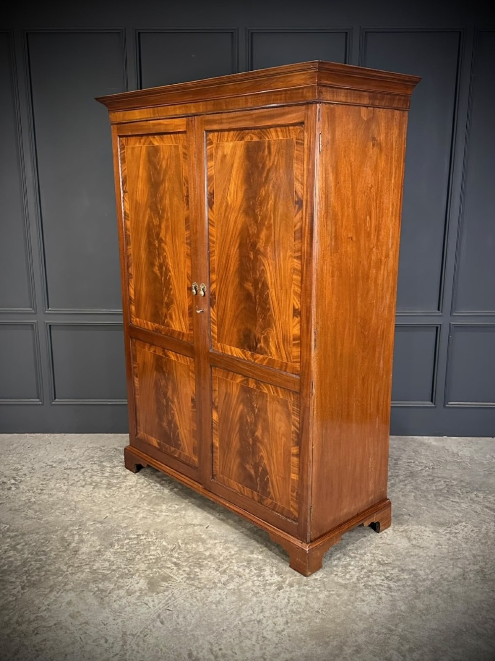 A tall Georgian style mahogany double wardrobe featuring flame mahogany door panels, a moulded cornice, and bracket feet. View VII