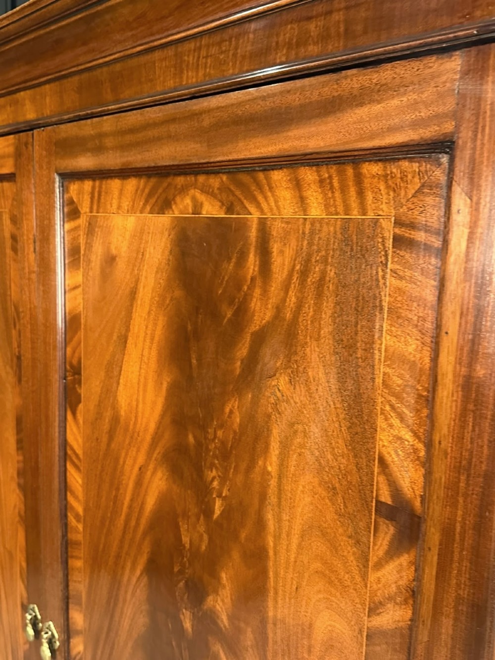 A tall Georgian style mahogany double wardrobe featuring flame mahogany door panels, a moulded cornice, and bracket feet. View VIII