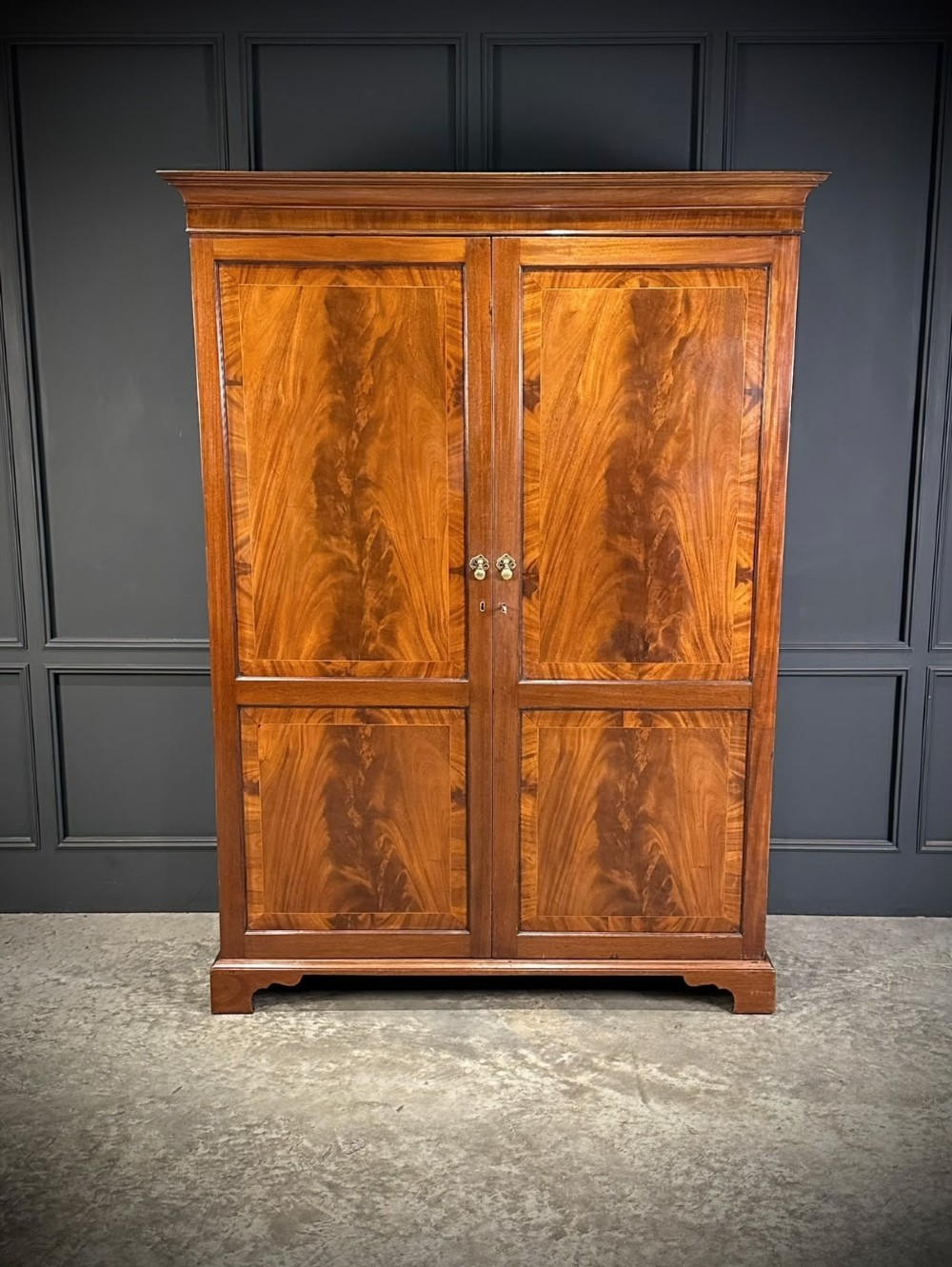 A tall Georgian style mahogany double wardrobe featuring flame mahogany door panels, a moulded cornice, and bracket feet. View IX