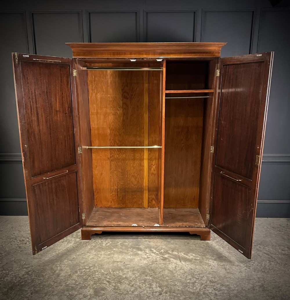 A tall Georgian style mahogany double wardrobe featuring flame mahogany door panels, a moulded cornice, and bracket feet. View X