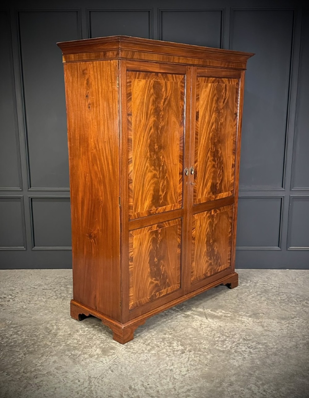 A tall Georgian style mahogany double wardrobe featuring flame mahogany door panels, a moulded cornice, and bracket feet.