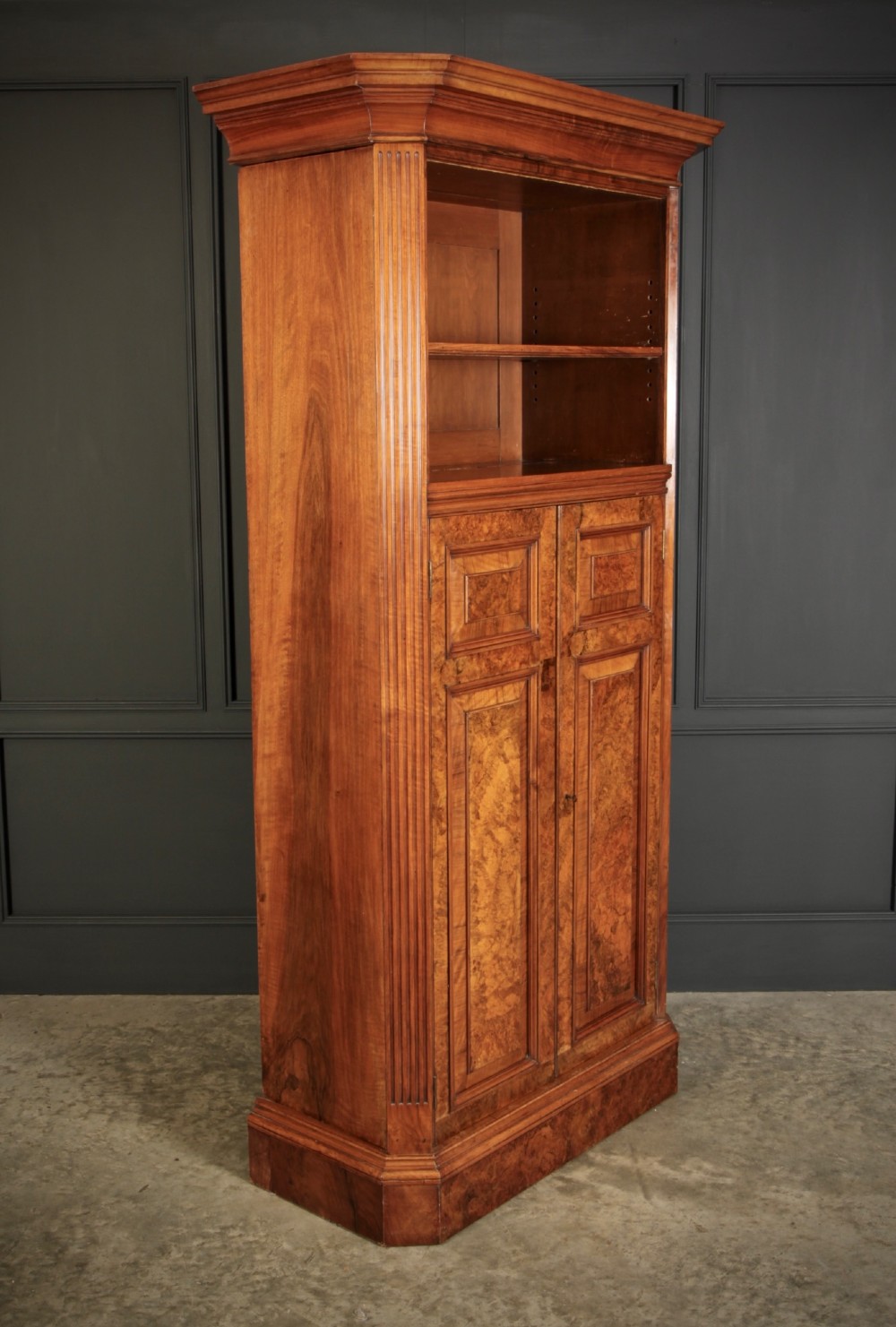 A tall Victorian burr walnut bookcase featuring open upper shelving over a double-door lower cupboard with fluted side pilasters.