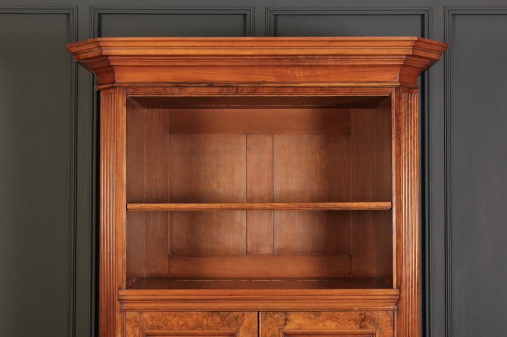 A tall Victorian burr walnut bookcase featuring open upper shelving over a double-door lower cupboard with fluted side pilasters. View III