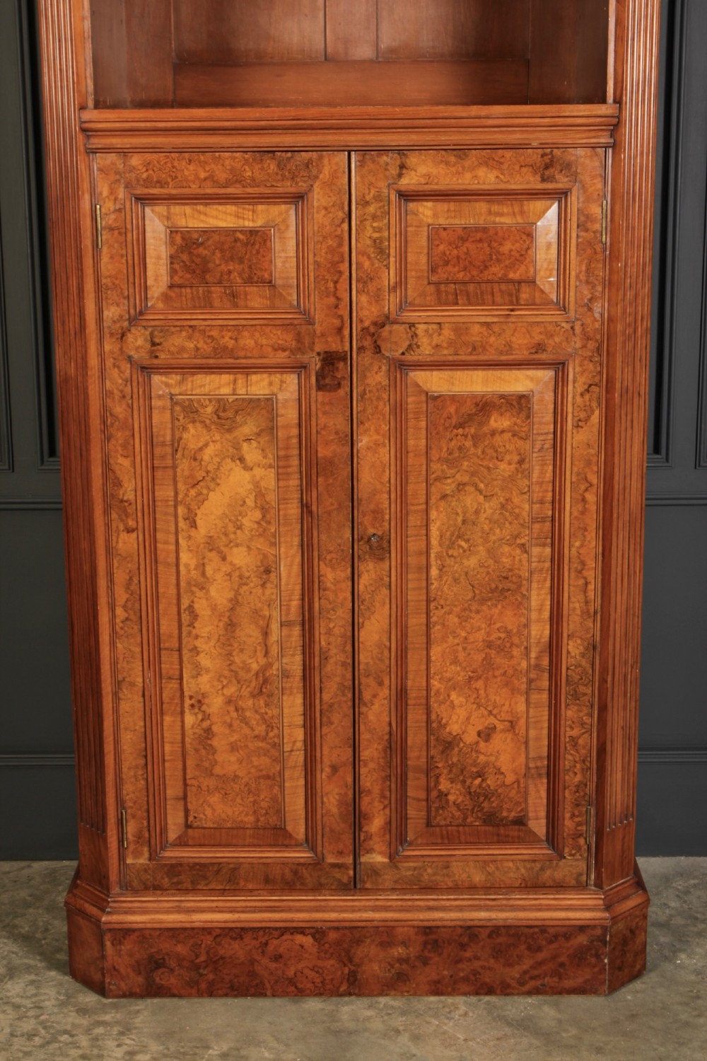 A tall Victorian burr walnut bookcase featuring open upper shelving over a double-door lower cupboard with fluted side pilasters. View IV