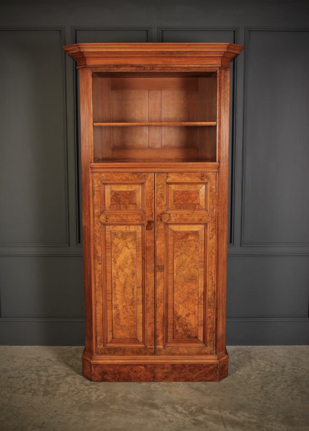 A tall Victorian burr walnut bookcase featuring open upper shelving over a double-door lower cupboard with fluted side pilasters. View VI