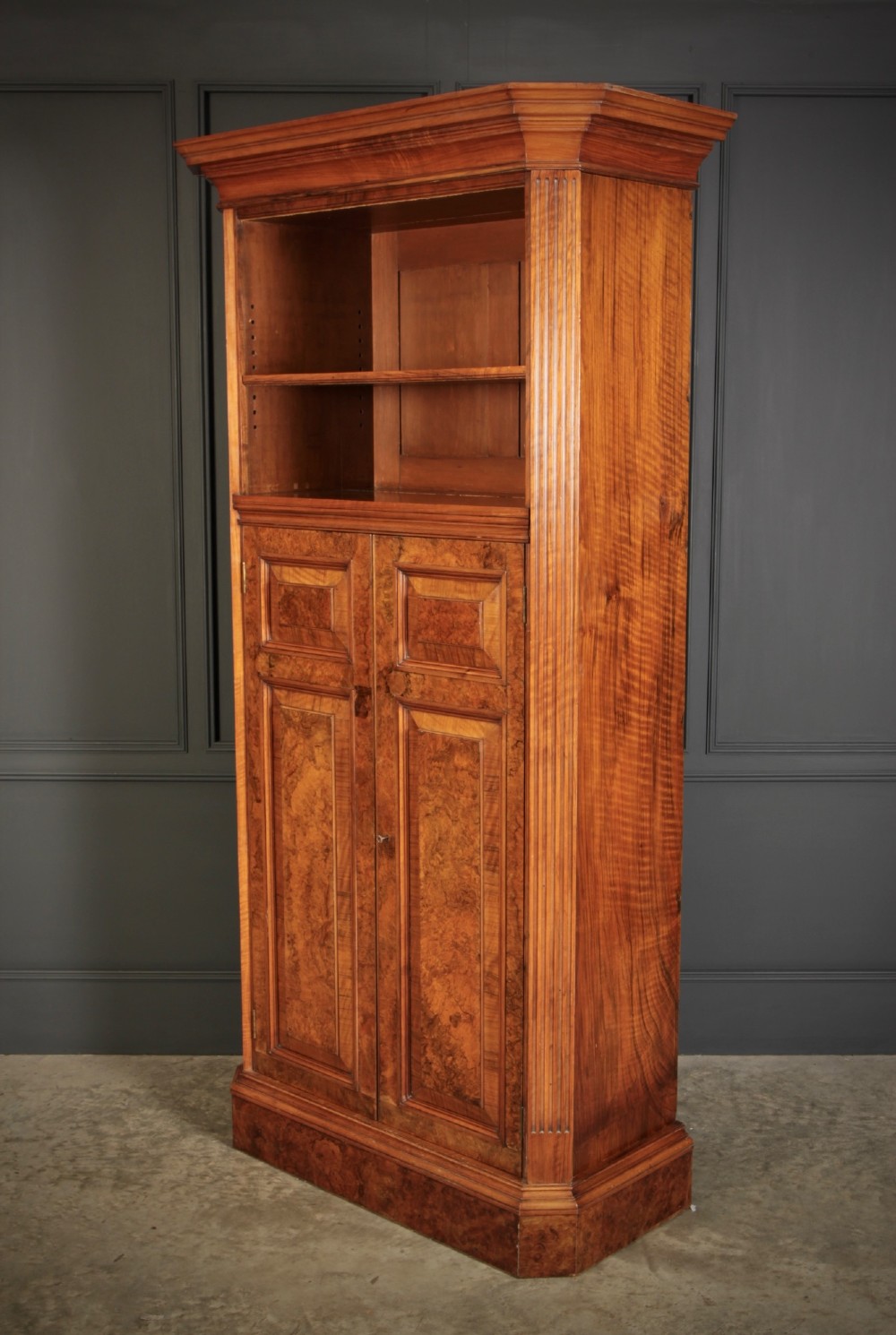 A tall Victorian burr walnut bookcase featuring open upper shelving over a double-door lower cupboard with fluted side pilasters. View IX