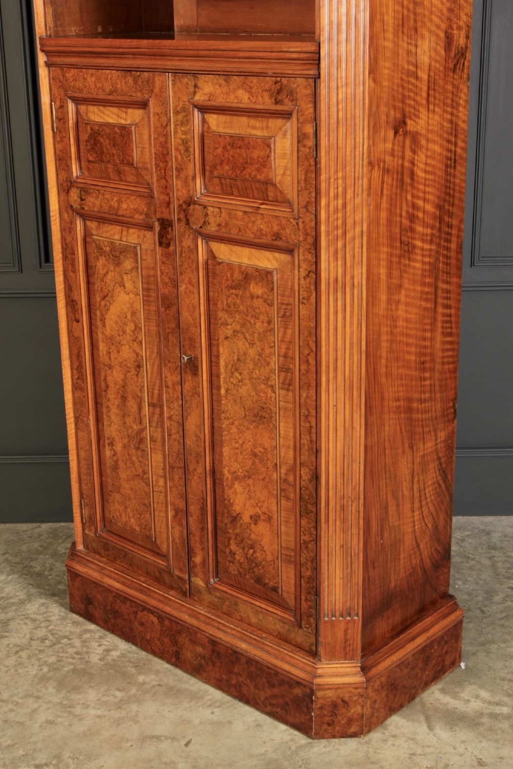 A tall Victorian burr walnut bookcase featuring open upper shelving over a double-door lower cupboard with fluted side pilasters. View X