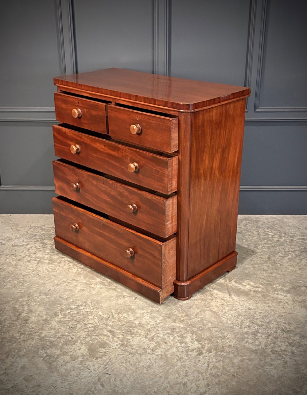 A Victorian mahogany chest of drawers with two short drawers over three long drawers, featuring turned wooden handles and a solid plinth base. View VII