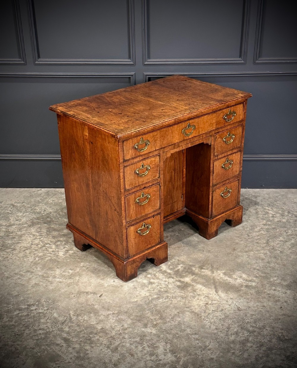 An 18th-century walnut kneehole desk featuring a flat top, multiple small drawers with brass drop handles, a recessed central cupboard, and bracket feet. View II