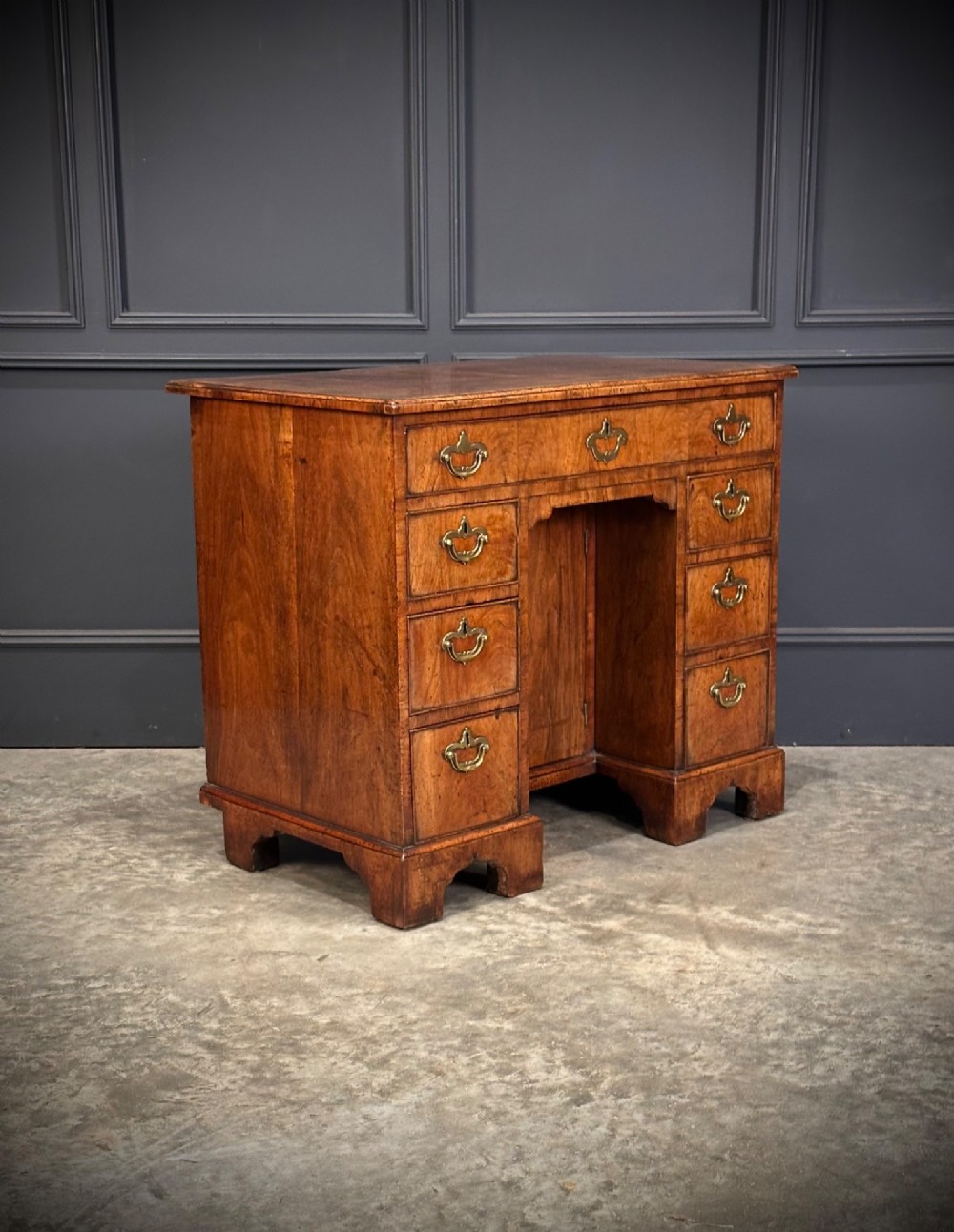 An 18th-century walnut kneehole desk featuring a flat top, multiple small drawers with brass drop handles, a recessed central cupboard, and bracket feet.
