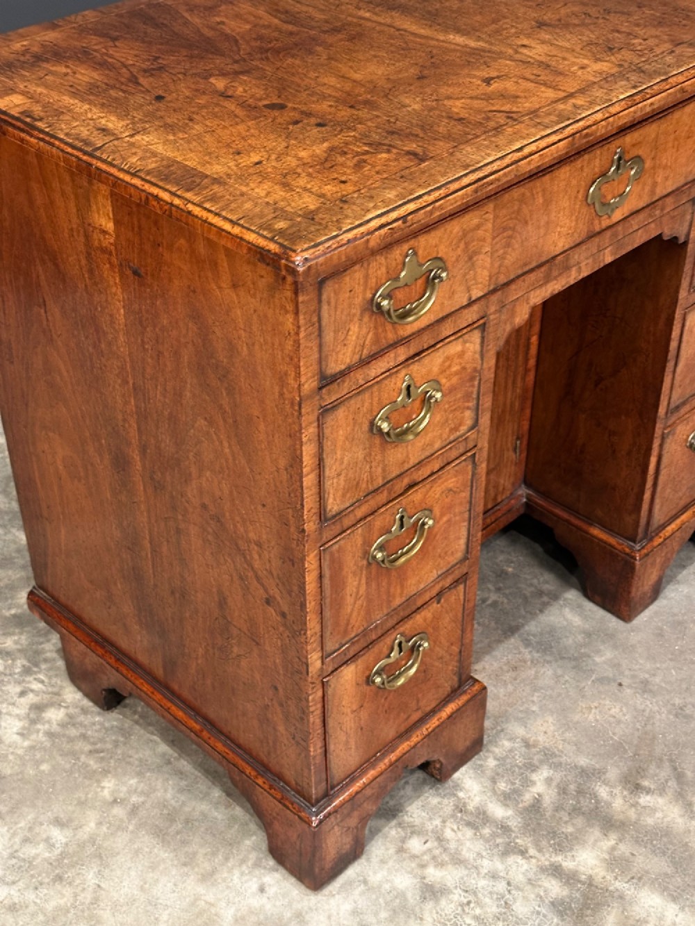 An 18th-century walnut kneehole desk featuring a flat top, multiple small drawers with brass drop handles, a recessed central cupboard, and bracket feet. View III