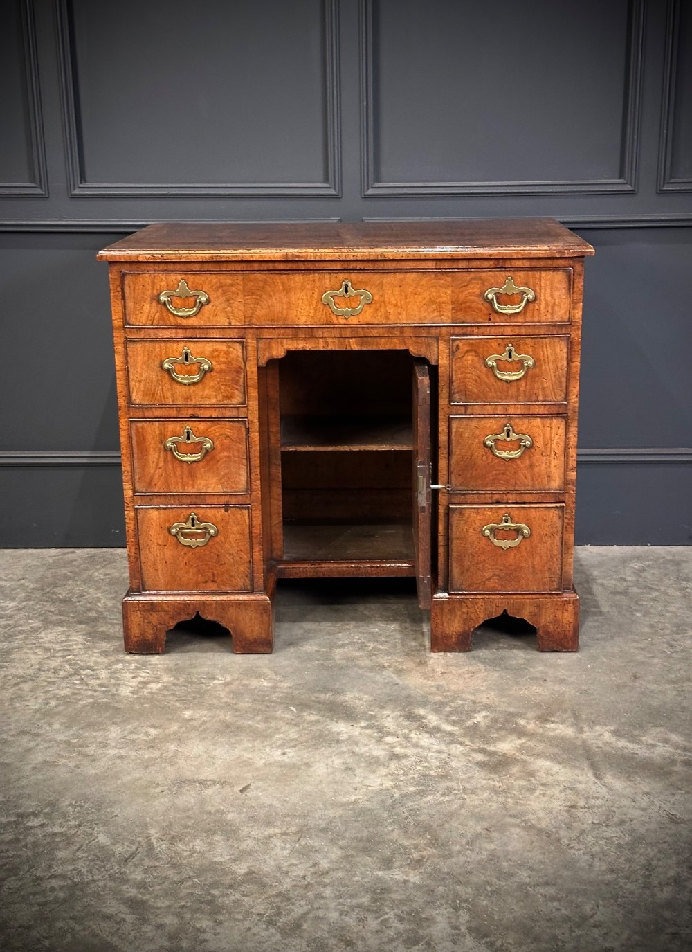 An 18th-century walnut kneehole desk featuring a flat top, multiple small drawers with brass drop handles, a recessed central cupboard, and bracket feet. View VIII