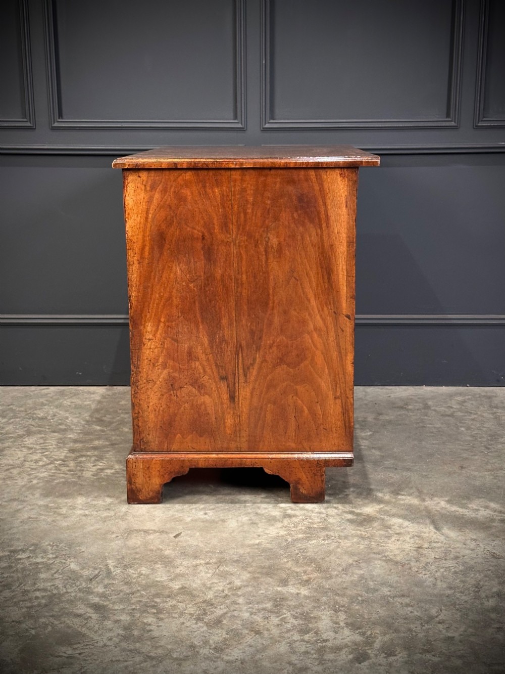 An 18th-century walnut kneehole desk featuring a flat top, multiple small drawers with brass drop handles, a recessed central cupboard, and bracket feet. View XII