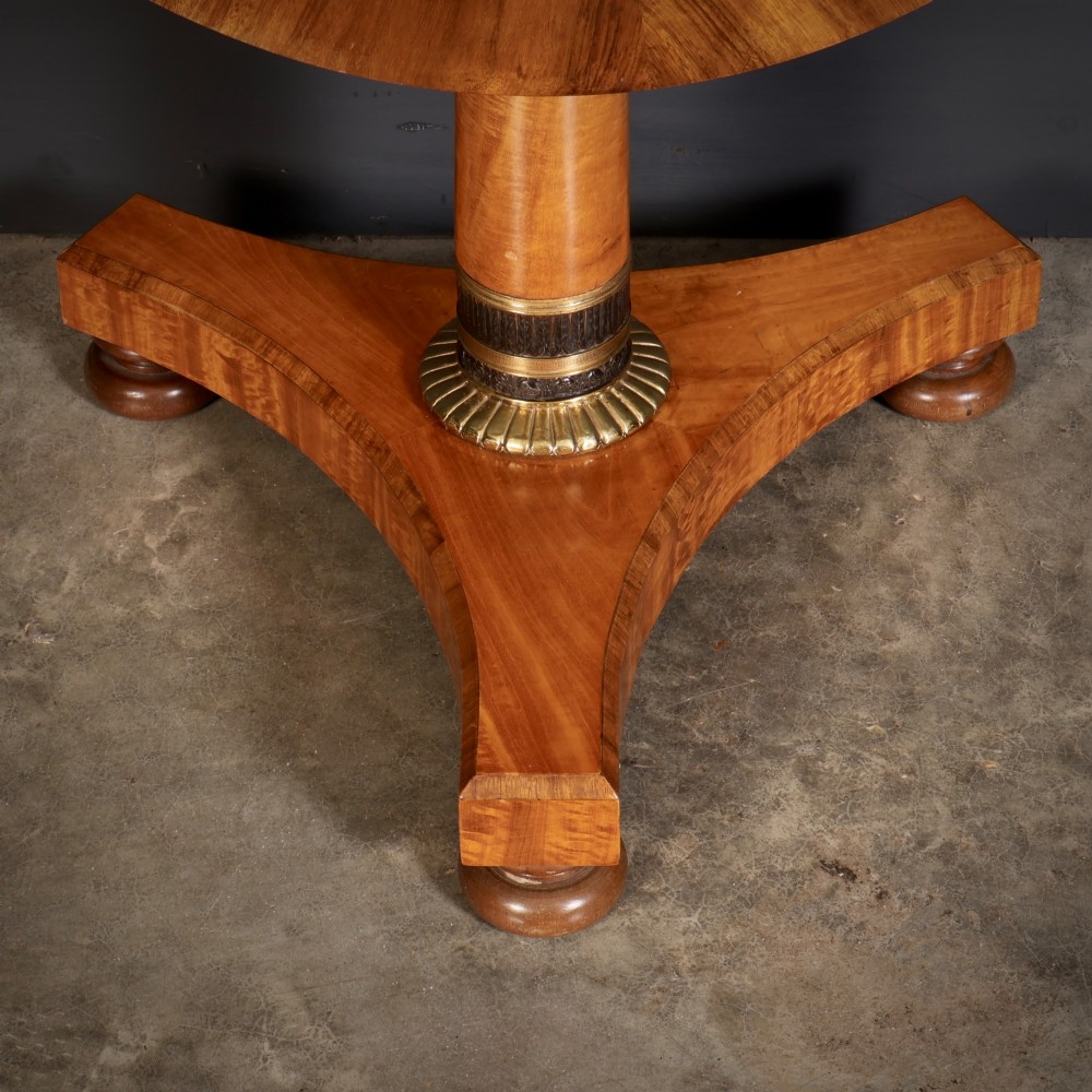 A circular antique satinwood occasional table featuring a crossbanded timber top, a central cylindrical pedestal with a brass mount, and a triform base on bun feet. View III