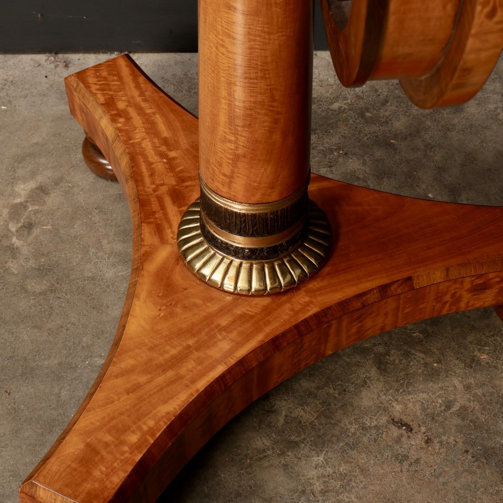 A circular antique satinwood occasional table featuring a crossbanded timber top, a central cylindrical pedestal with a brass mount, and a triform base on bun feet. View VIII
