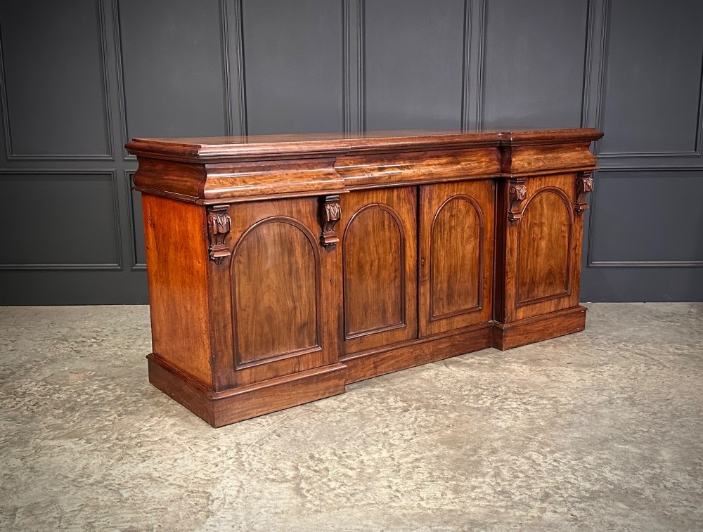 A Victorian mahogany four-door breakfront sideboard featuring arched panel doors, carved support brackets, and a long flat top surface. View II