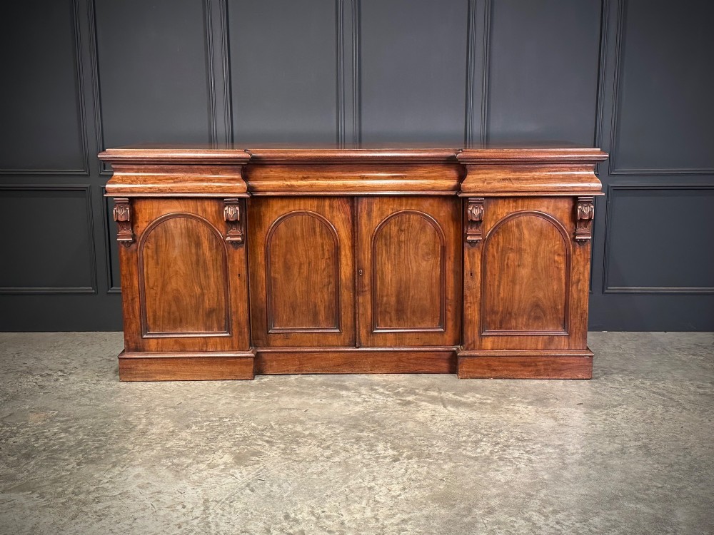 A Victorian mahogany four-door breakfront sideboard featuring arched panel doors, carved support brackets, and a long flat top surface.