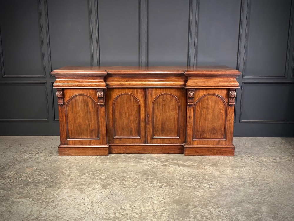 A Victorian mahogany four-door breakfront sideboard featuring arched panel doors, carved support brackets, and a long flat top surface. View VI