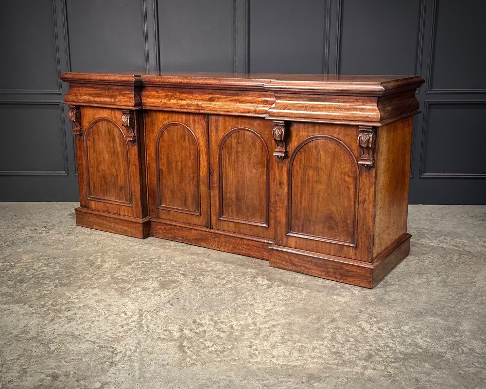 A Victorian mahogany four-door breakfront sideboard featuring arched panel doors, carved support brackets, and a long flat top surface. View IX