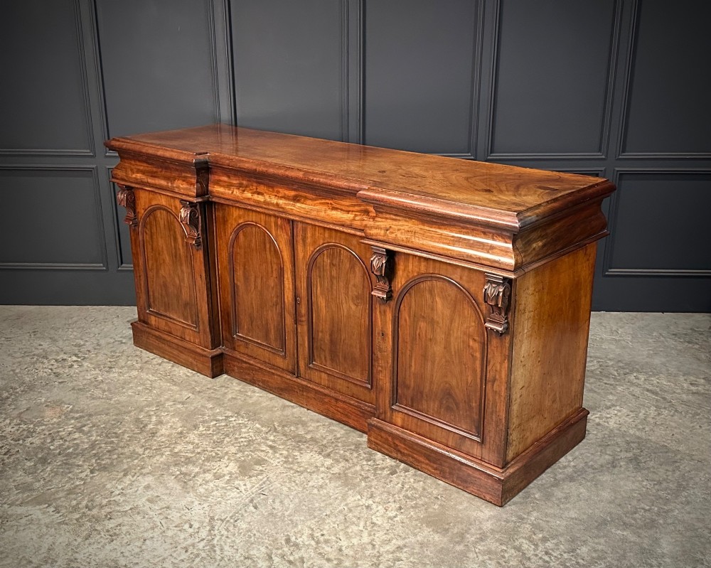 A Victorian mahogany four-door breakfront sideboard featuring arched panel doors, carved support brackets, and a long flat top surface. View X