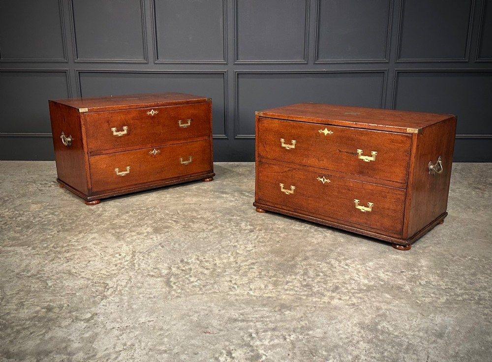 A pair of low two-drawer Regency teak military campaign chests featuring recessed brass handles, flush corner brackets, and turnip feet.